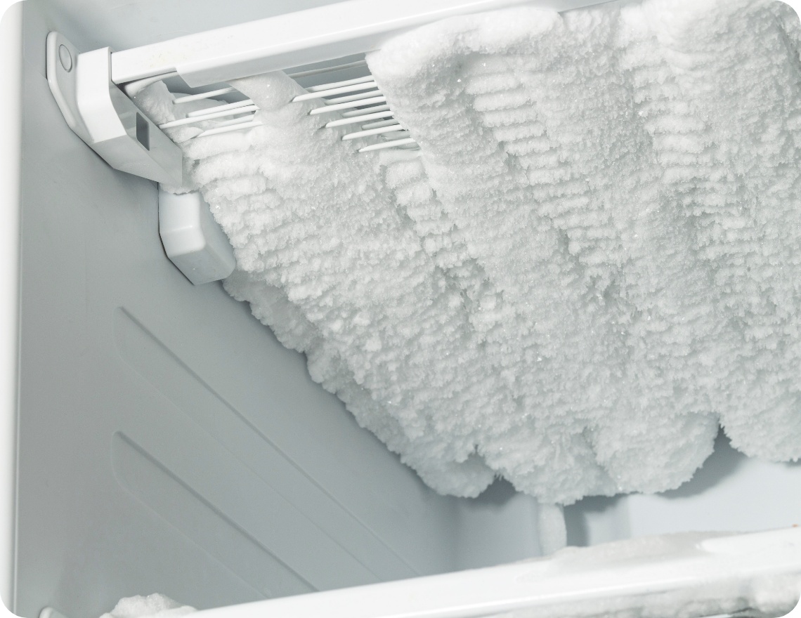 Stark vereister Gefrierschrank von innen mit dicker Eisschicht an den Kühlrippen und Wänden.