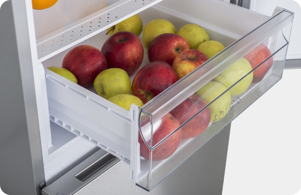 Offene Gemüseschublade eines Kühlschranks mit roten und gelben Äpfeln.