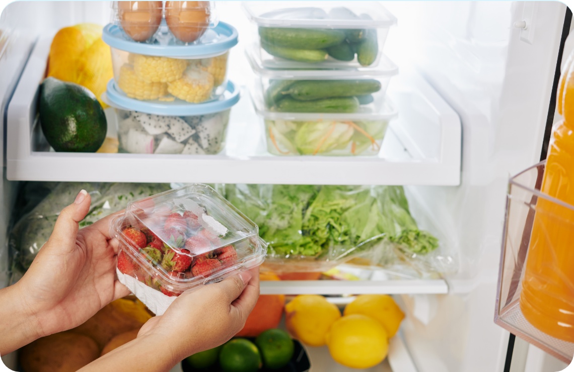 Eine Person hält eine Schale mit Erdbeeren vor einem gut organisierten Kühlschrank mit frischem Obst, Gemüse und Lebensmitteln.