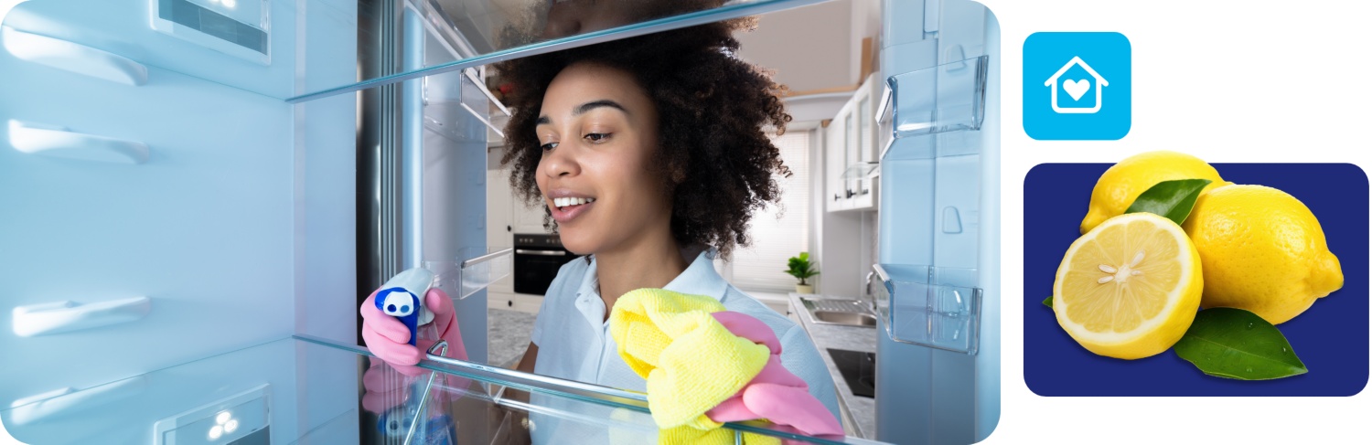 Frau mit Handschuhen reinigt einen leeren Kühlschrank mit Sprühreiniger und gelbem Mikrofasertuch in moderner Küche.