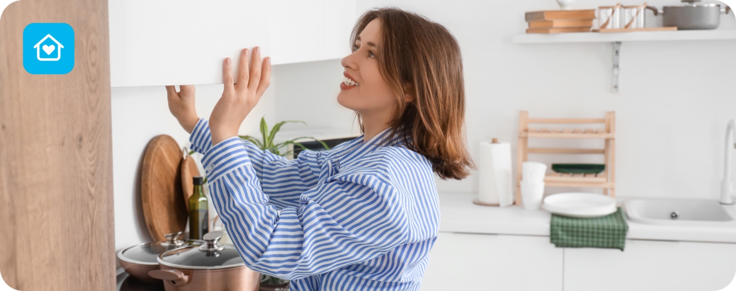 Frau in blau-weiß gestreifter Bluse öffnet einen Küchenschrank in einer modernen weißen Küche.