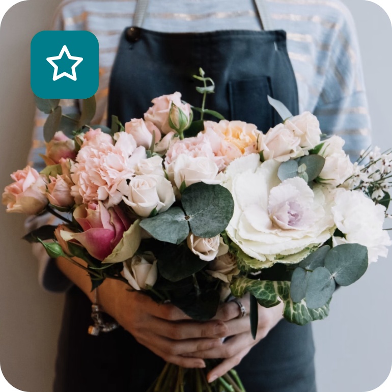 Floristin mit dunkelgrüner Schürze hält Blumenstrauß aus weißen und hellrosafarbenen Blumen.