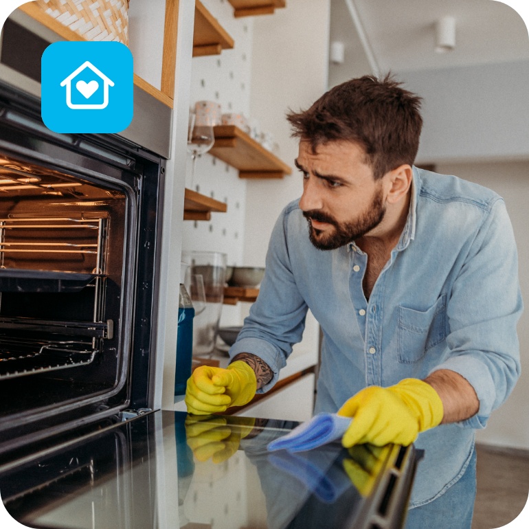 Ein Mann steht mit gelben Haushaltshandschuhen vor dem geöffneten Backofen, um ihn zu reinigen.