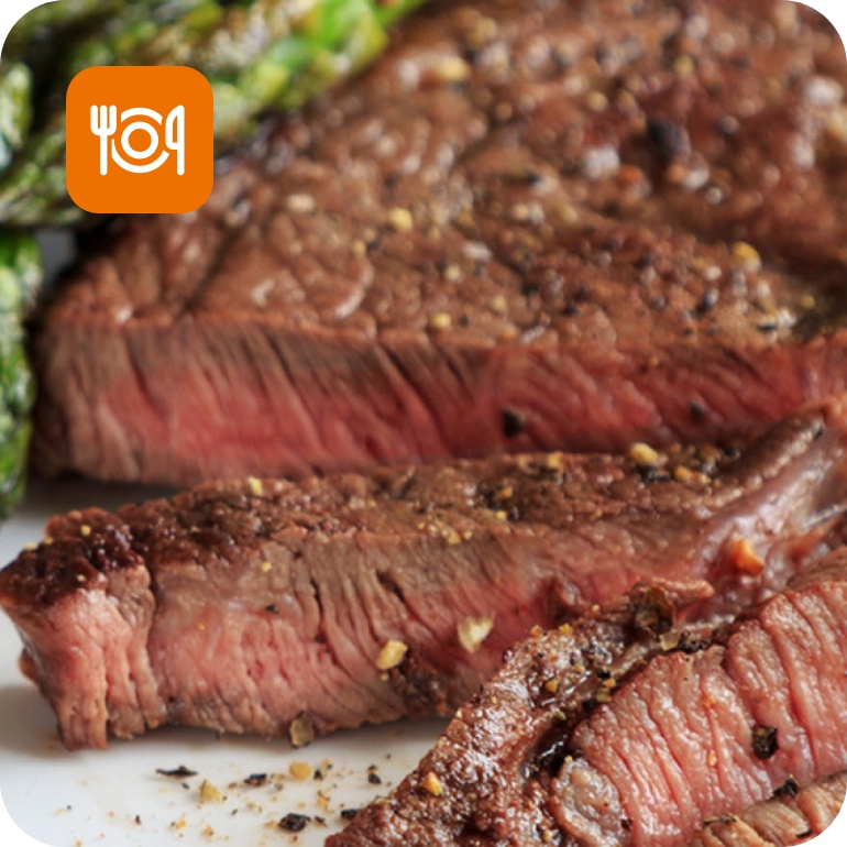 Medium-rare gegrilltes Steak mit Gewürzen, serviert mit grünem Spargel auf einem weißen Teller. Saftig und aromatisch.