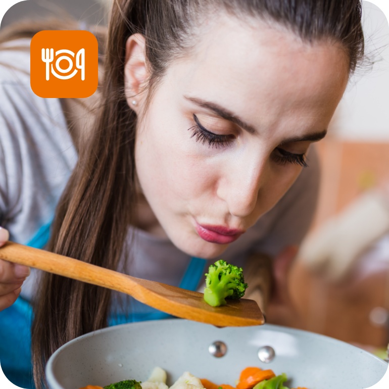 Frau probiert mit einem Holzlöffel gedünstetes Gemüse aus einer Pfanne.