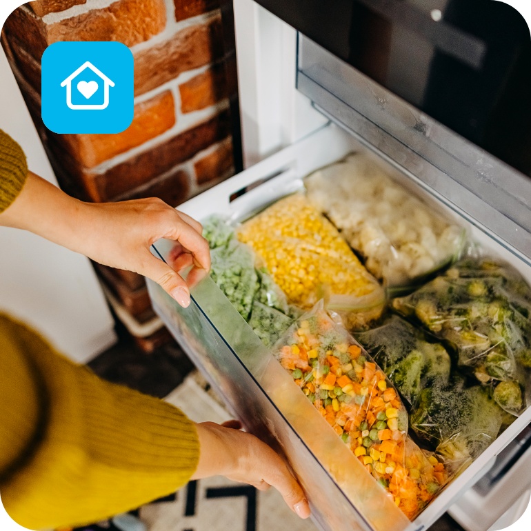 Person öffnet ein Gefrierfach, das mit abgepacktem Gemüse gefüllt ist.