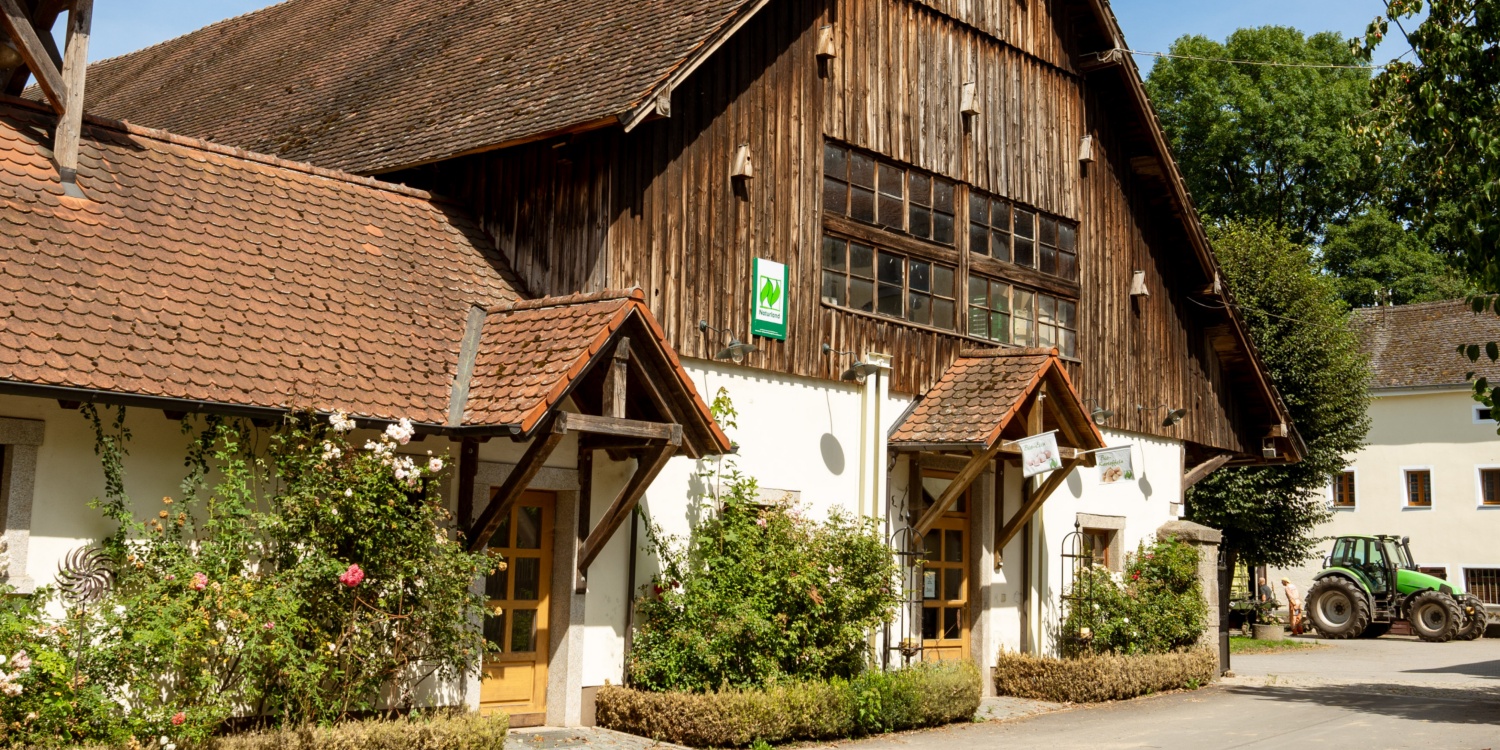 Ein traditionelles Bauernhofgebäude mit hölzernem Giebel, Ziegeldach und begrünten Fassaden, ein Traktor steht im Hof.