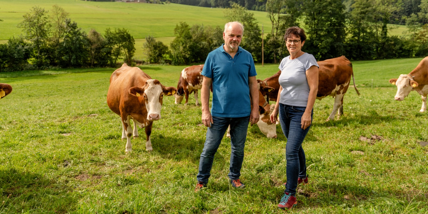 Herr und Frau Lechner stehen gemeinsam auf ihrer Wiese, im Hintergrund Kühe.