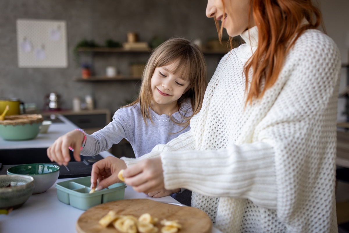 Mutter und Tochter bereiten gemeinsam geschnittene Bananen zu.