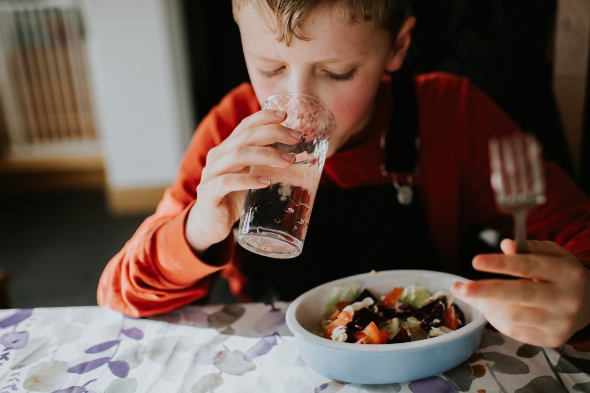 Junge trinkt Wasser aus dem Glas und isst dazu einen frischen Salat.