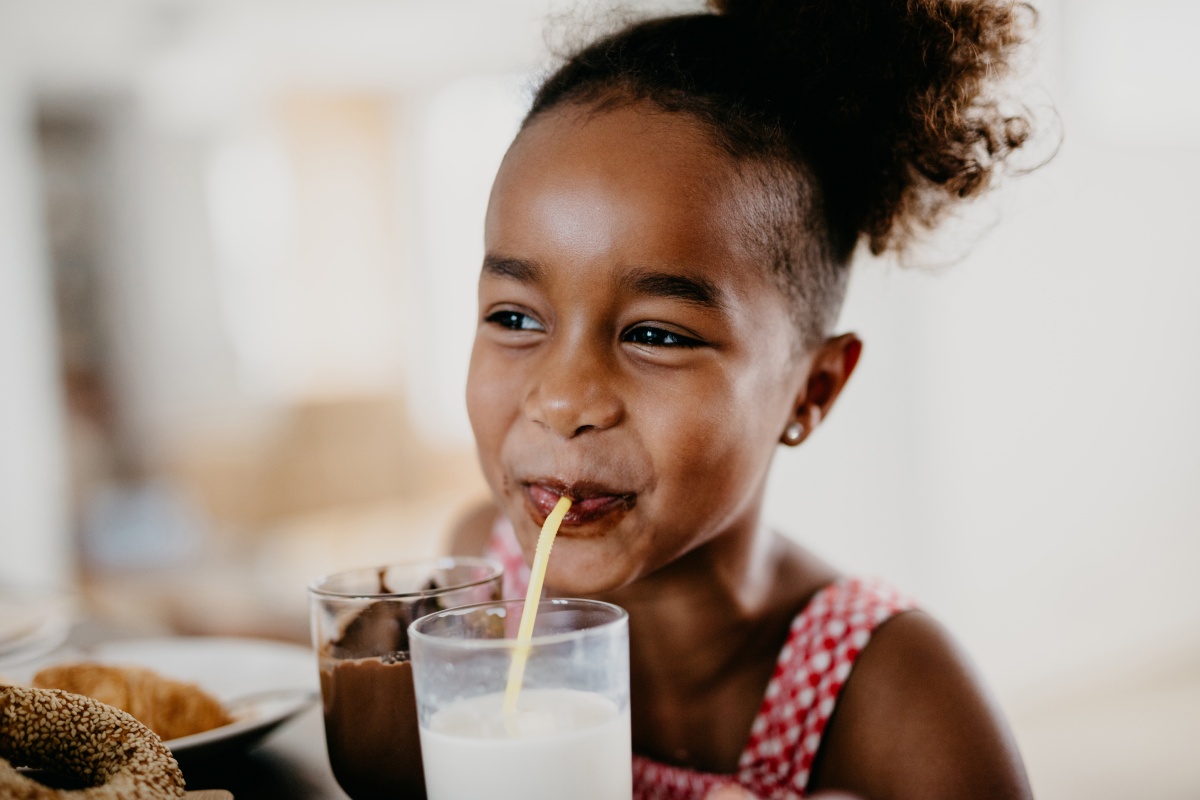 Mädchen trinkt fröhlich Milch aus einem Glas mit dem Strohhalm.