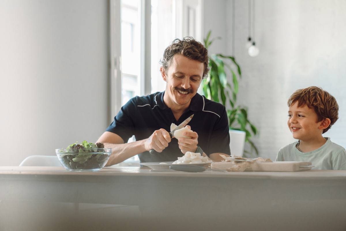 Vater schneidet Gemüse, während sein Sohn dabei zusieht.