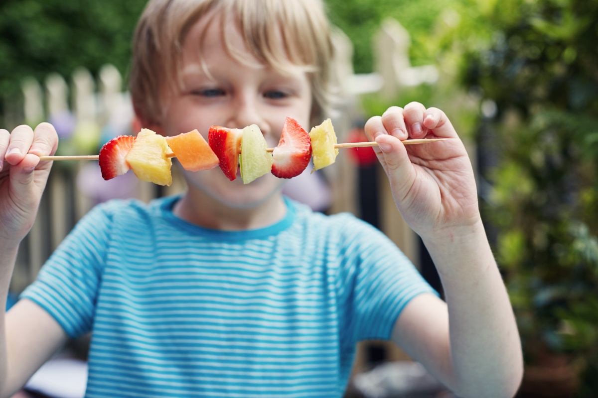 Junge hält einen bunten Fruchtspieß mit Erdbeeren, Ananas und Melone.