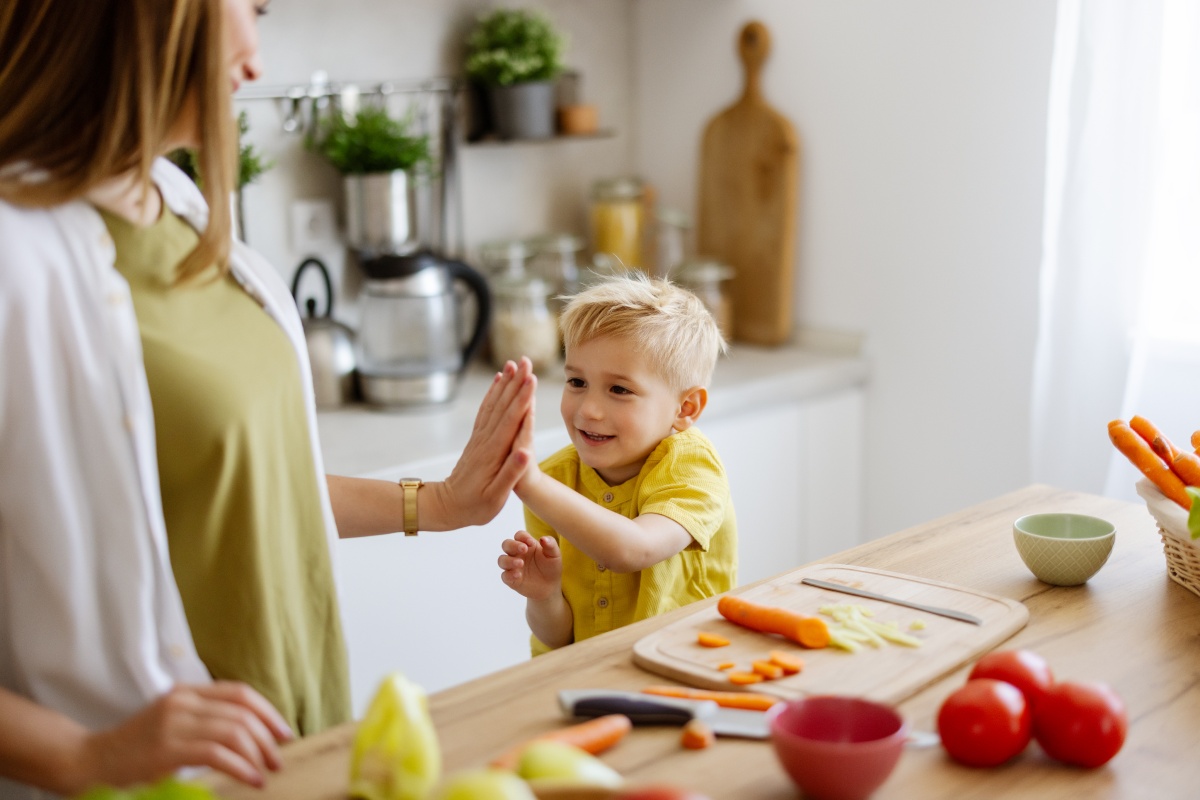 Mutter und Kind geben sich in der Küche ein High-Five, beim Zubereiten von Gemüse in der Küche.