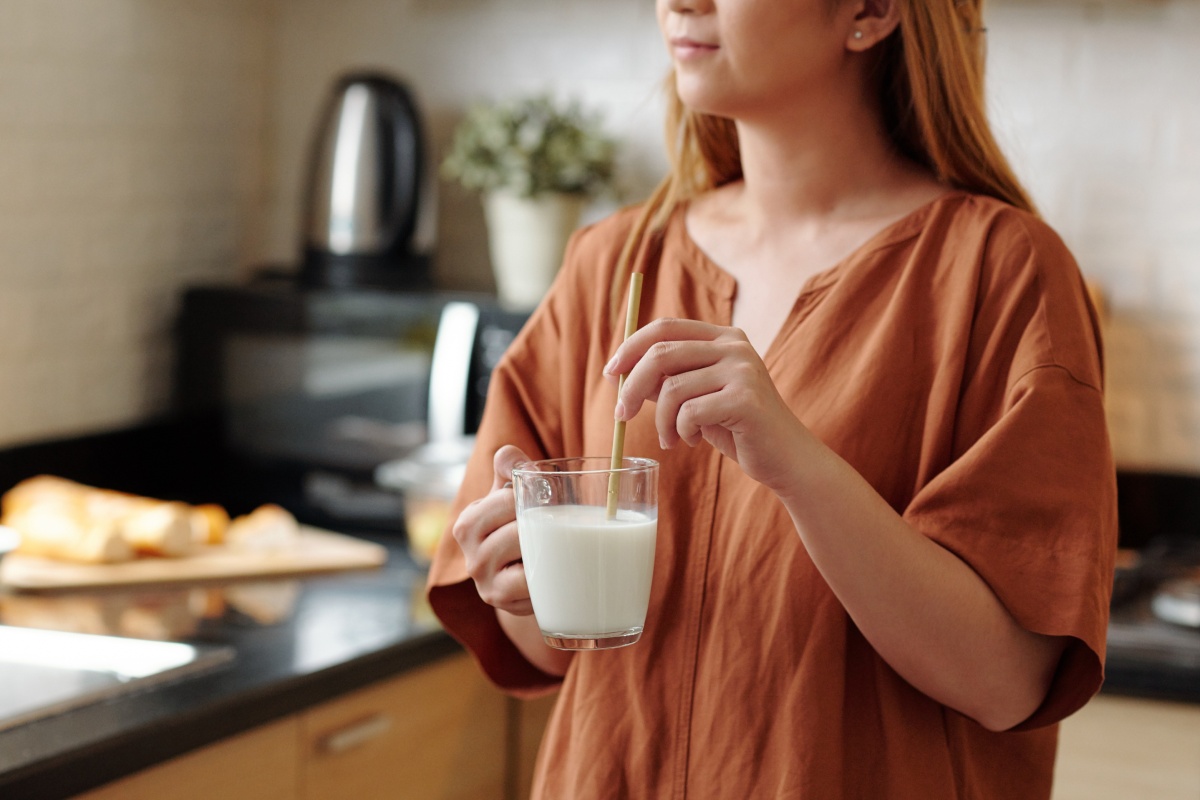 Frau in brauner Bluse steht in einer modernen Küche und rührt mit einem Strohlhalm in einem Glas Milch.