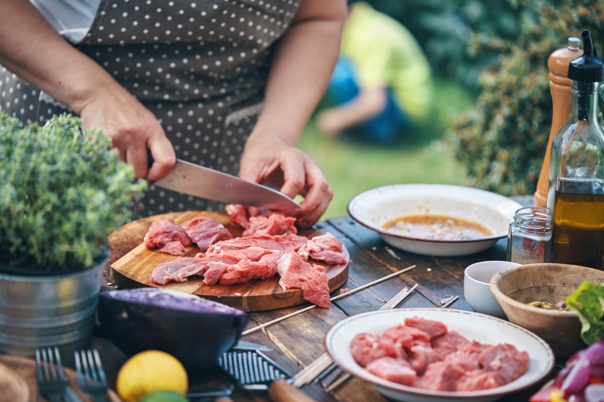 Person schneidet rohes Fleisch auf einem Holzbrett.
