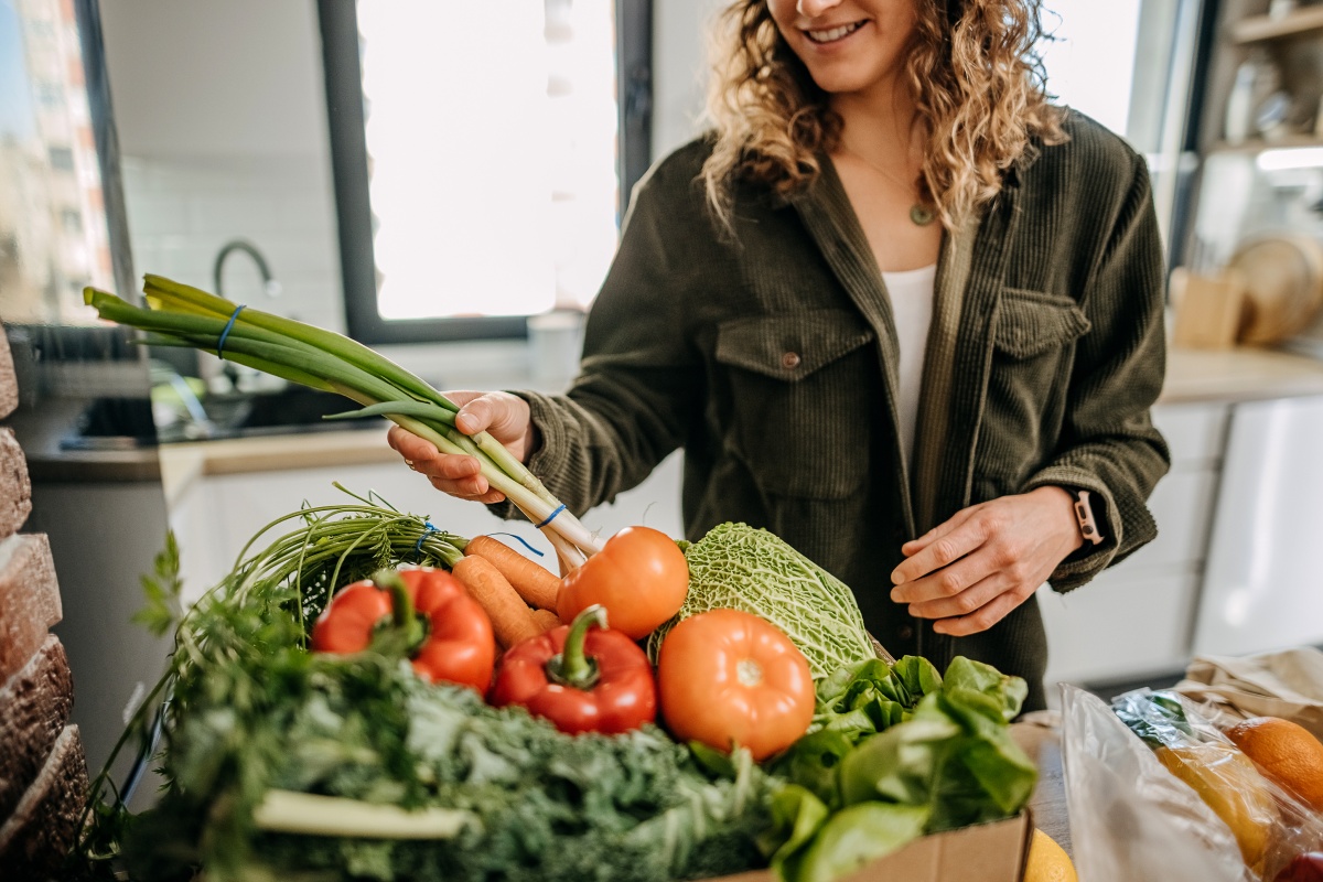Person nimmt ein Bund Frühlingszwiebeln aus eine Gemüsekiste.