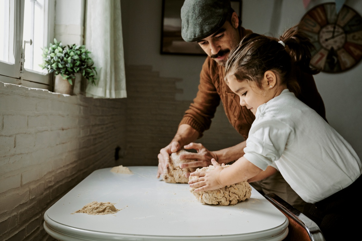 Vater und Kind kneten zusammen Teig auf einem Tisch.