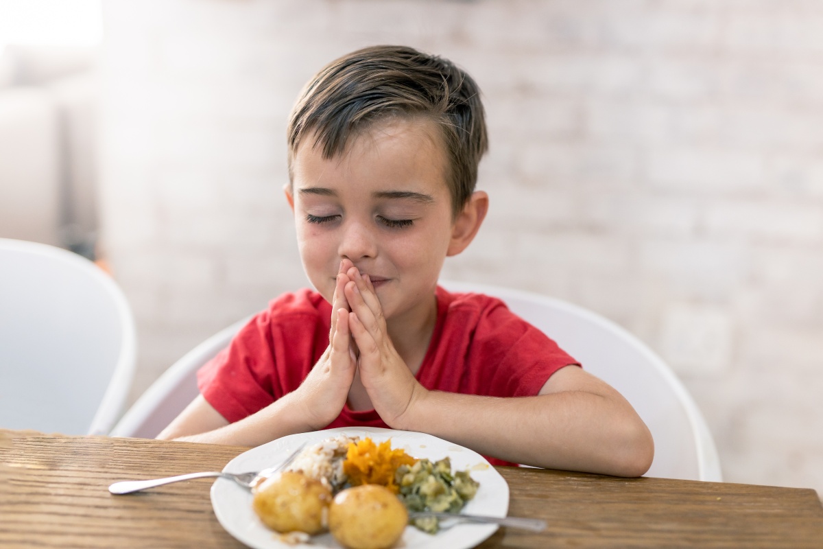 Kind betet vor dem Essen mit geschlossenen Augen.