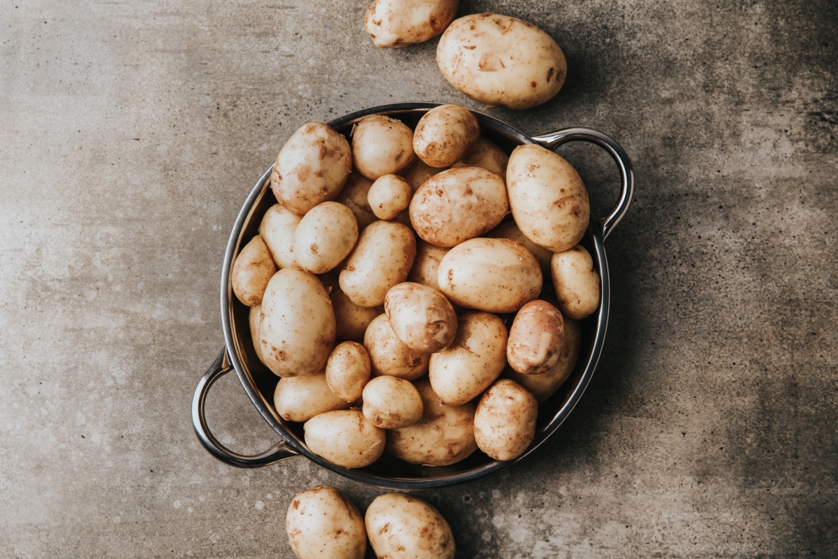 Frische, ungekochte Kartoffeln in einem Sieb auf einer melierten Tischplatte.