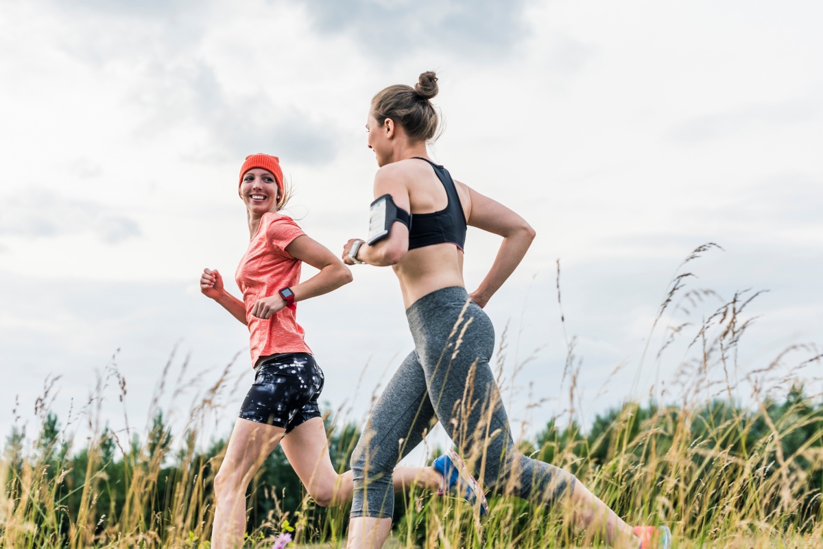 Zwei Frauen joggen gemeinsam durch ein Feld bei bewölktem Himmel.