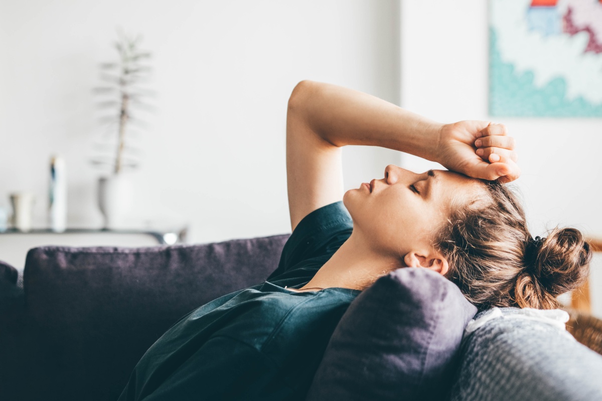 Frau lehnt erschöpft auf einem Sofa und hält ihre Hand an die Stirn.