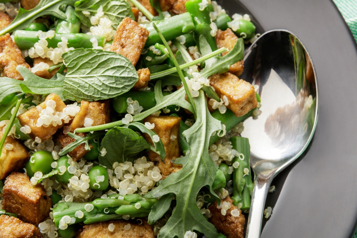 Quinoasalat mit gebratenem Tofu, grünen Bohnen, Rucola und Minze, angerichtet auf einem Teller mit einem Löffel.