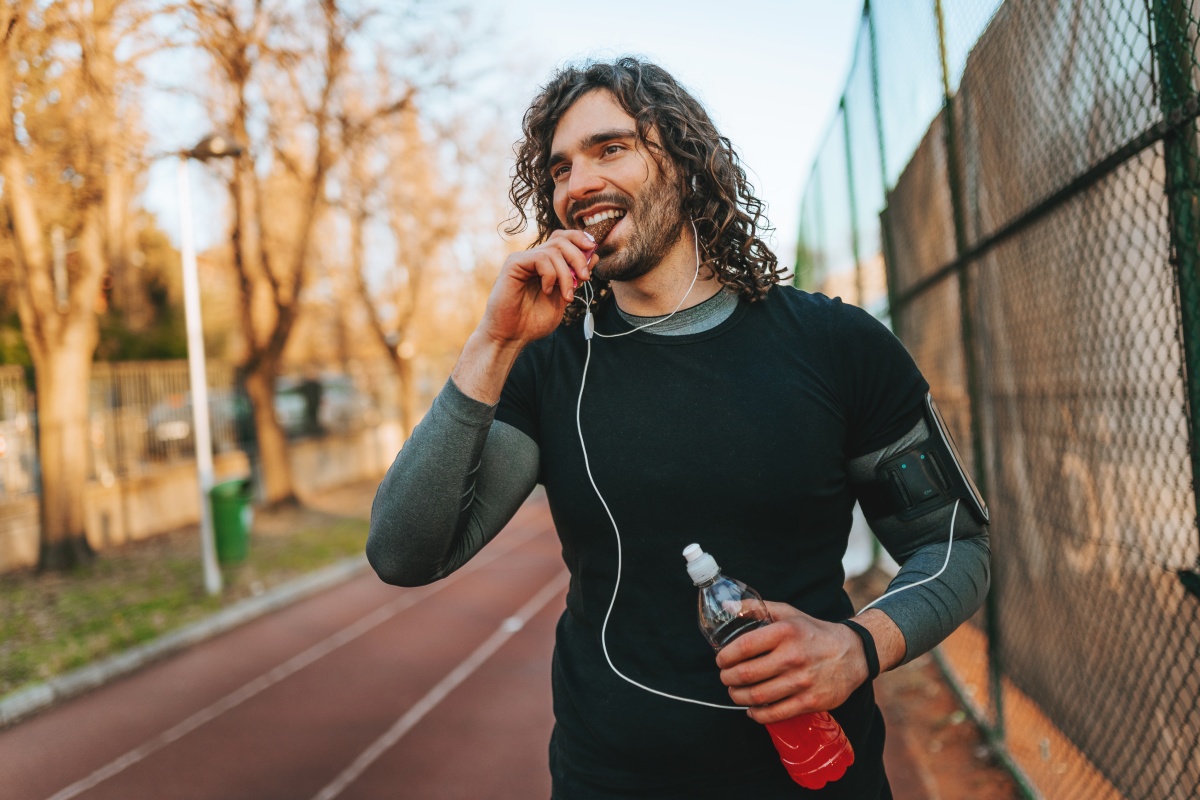 Jogger beißt in einen Energieriegel und hält eine Getränkeflasche, während er auf einer Laufbahn trainiert.
