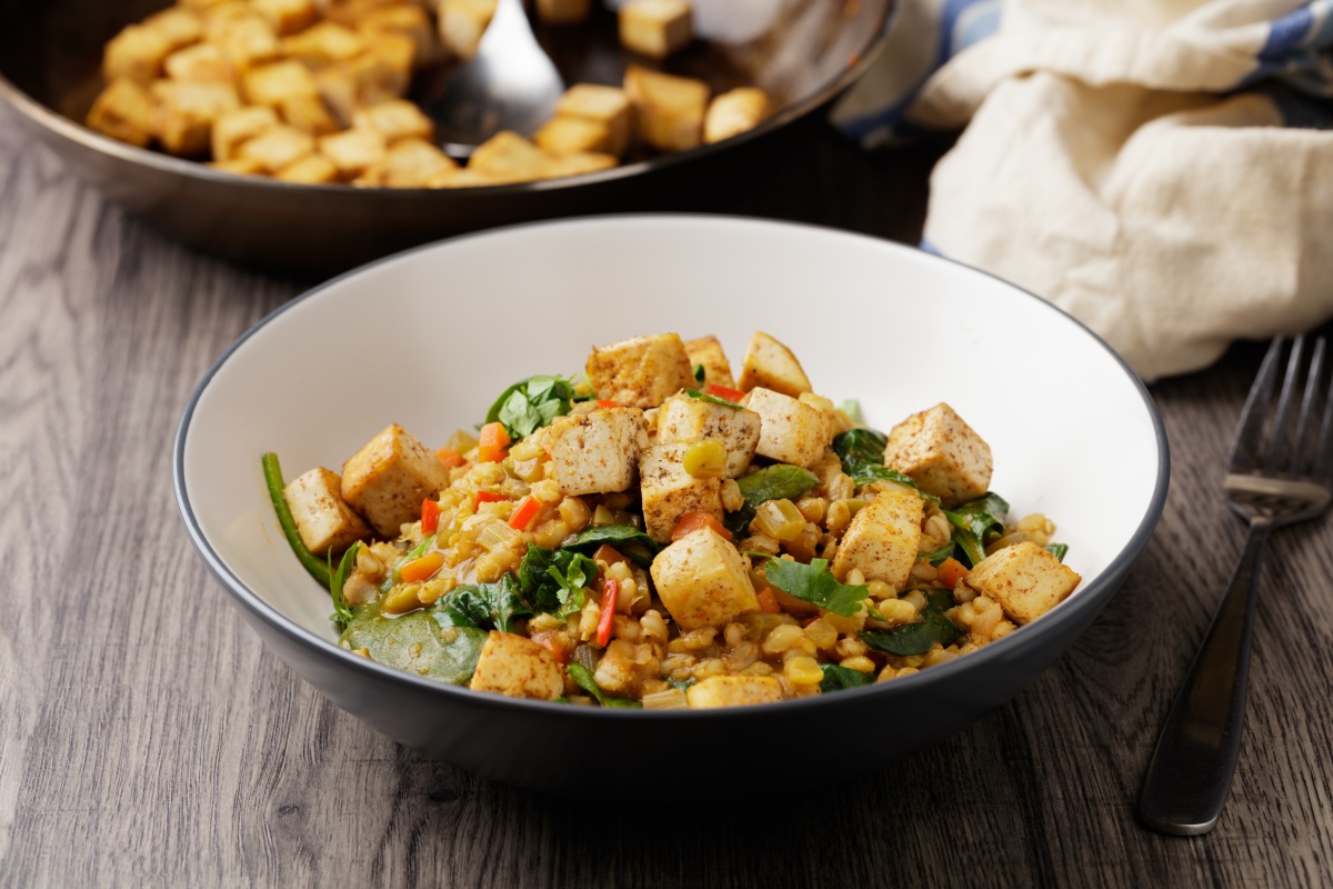 Schüssel mit gebratenem Tofu, Gemüse und Linsen, serviert auf einem Holztisch.