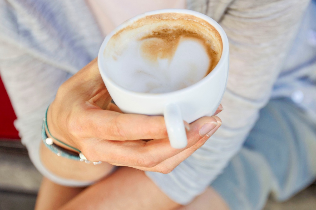 Eine Hand hält eine Tasse Cappuccino.