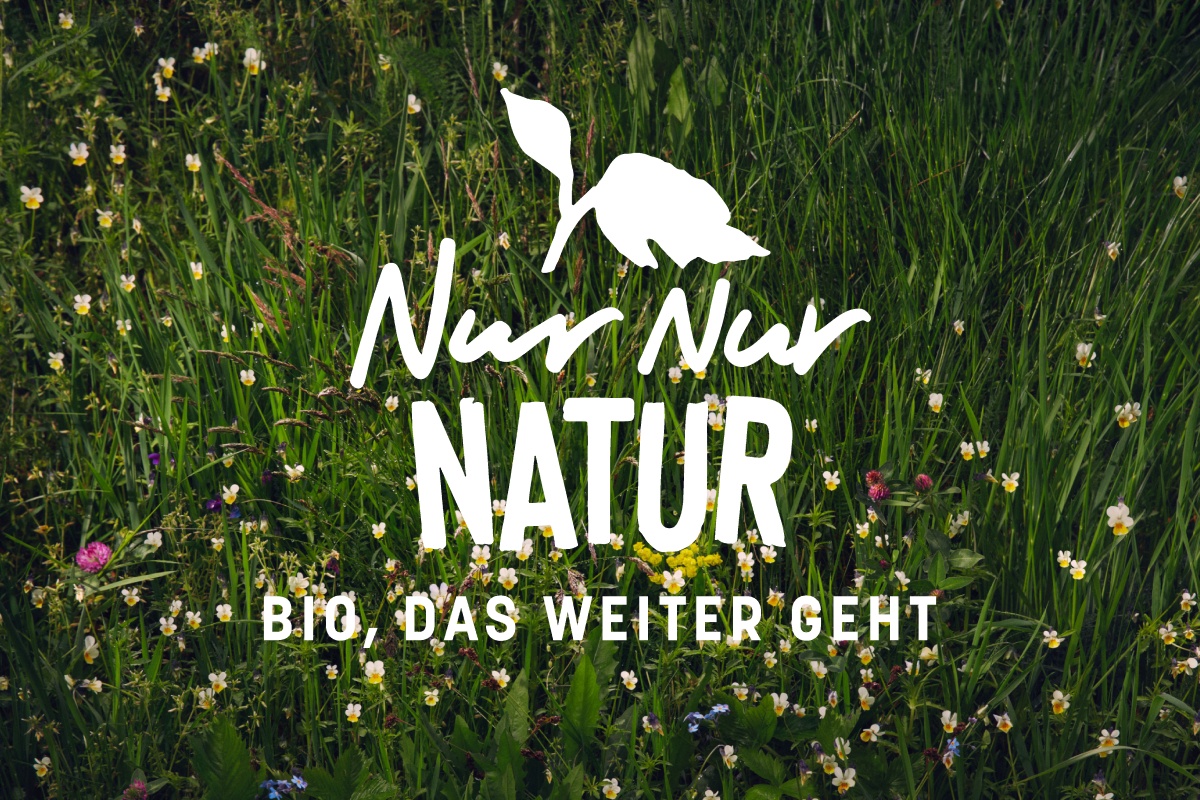 Das NUR NUR NATUR Logo vor dem Hintergrund einer Wiese.