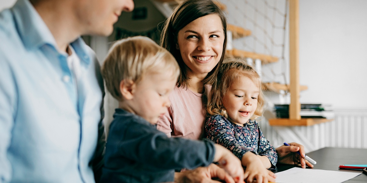 Vater und Mutter mit je einem Kind auf dem Arm lächeln sich an.