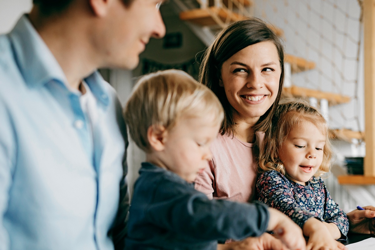 Vater und Mutter mit je einem Kind auf dem Arm lächeln sich an.
