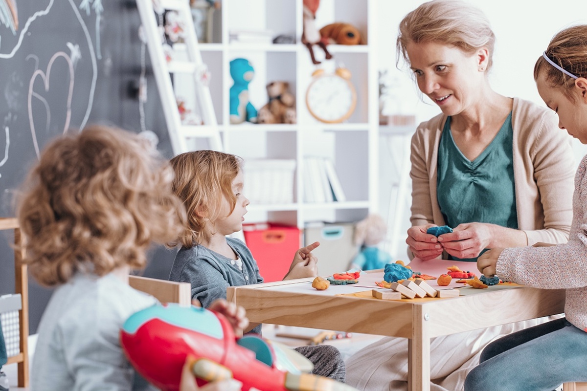 Eine Frau und drei Kleinkinder spielen mit Knete an einem Tisch.