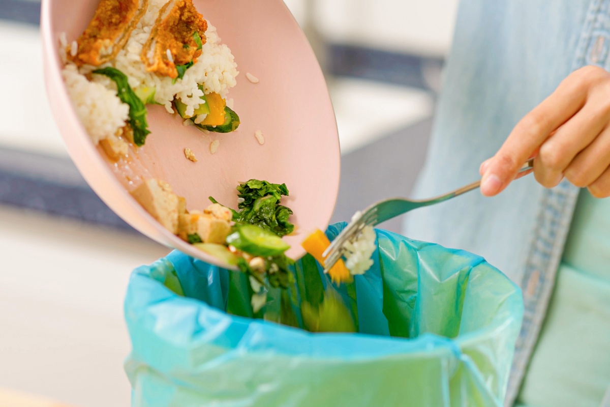 Eine Person ist gerade dabei größere Essensreste von Ihrem Teller in den Mülleimer zu leeren.