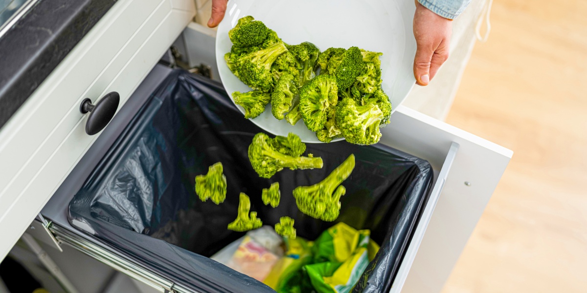 Eine Person leert eine große Portion noch essbarer Reste von Brokkoli in den Mülleimer.