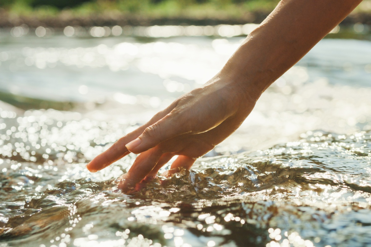 Ein Hand streift durch das Wasser eins Bachlaufs.