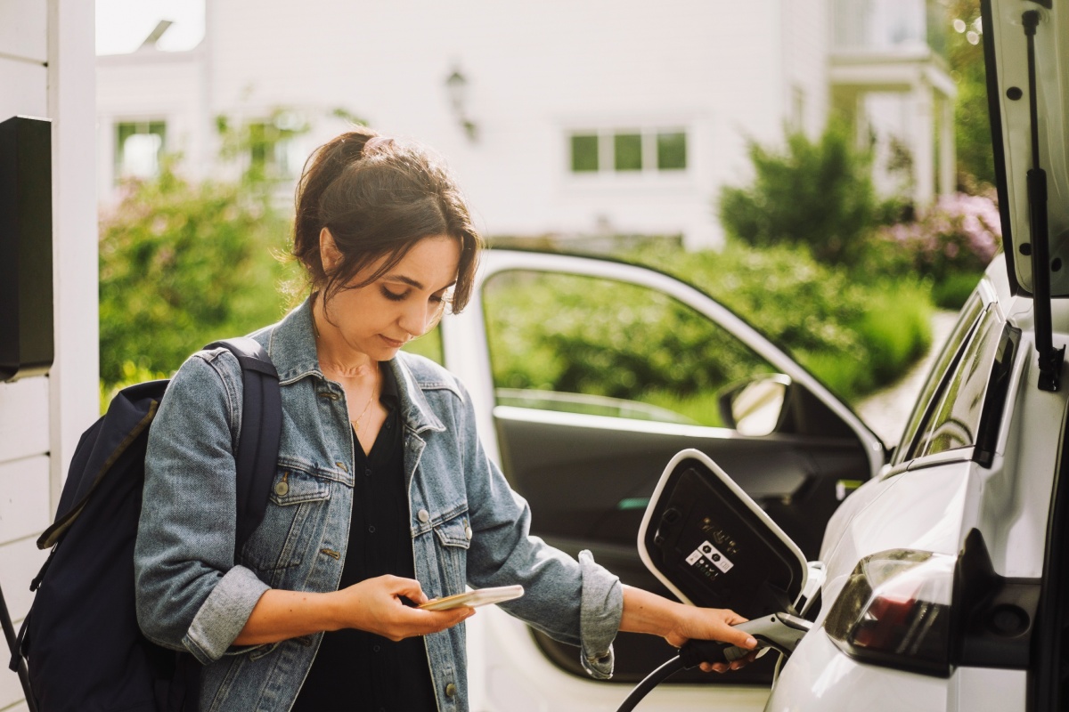 Eine junge Frau guckt beim Tanken an der ALDI SÜD Ladestation auf die Handy-App.