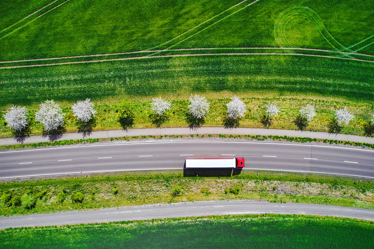 LKW auf einer Landstraße zwischen grünen Feldern.