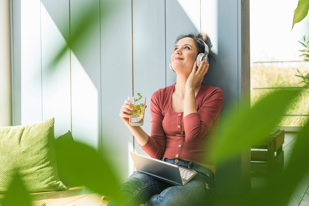 Eine junge Frau sitzt mit Laptop und Kopfhörern in der Sonne.