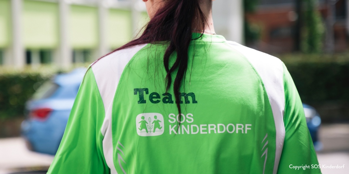 Nahaufnahme des Rückens einer Frau, die ein grünes SOS-Kinderdorf Teamshirt trägt.