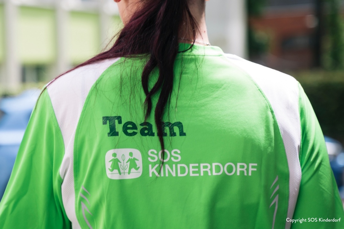Nahaufnahme des Rückens einer Frau, die ein grünes SOS-Kinderdorf Teamshirt trägt.