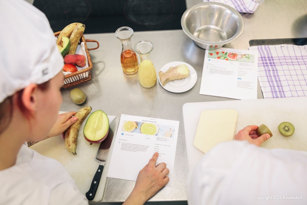 Kind in einer Küche studiert Rezept neben frischen Zutaten.