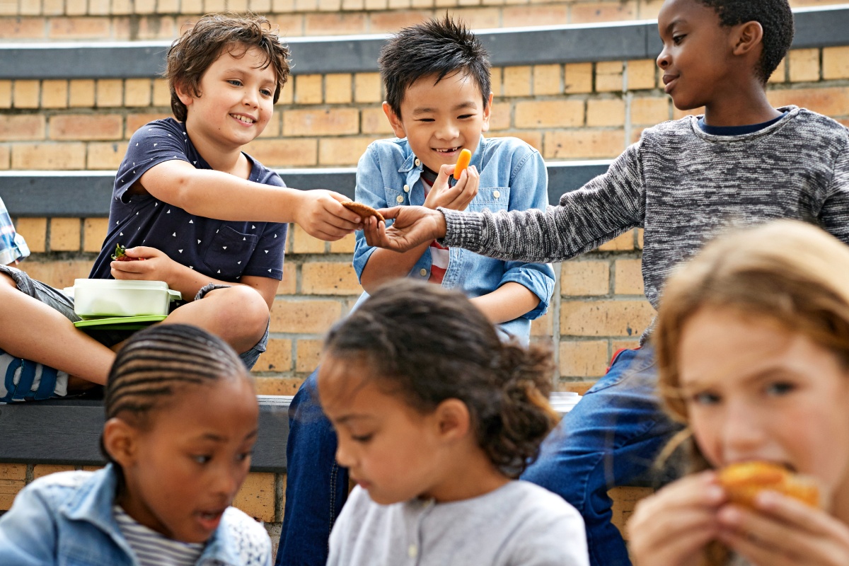 Kinder teilen sich ihre Pausenbrote auf einer Bank.