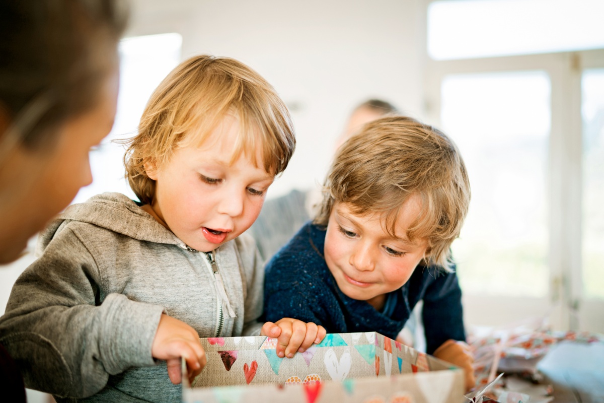 Zwei kleine Kinder halten eine Geschenkbox und schauen erfreut hinein.