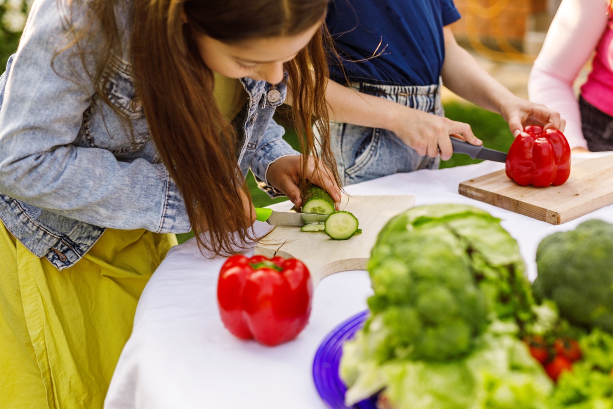 Ein Mädchen und im Hintergrund weitere Kinder, die an einem Tisch Gurken und rote Paprikas schneiden.