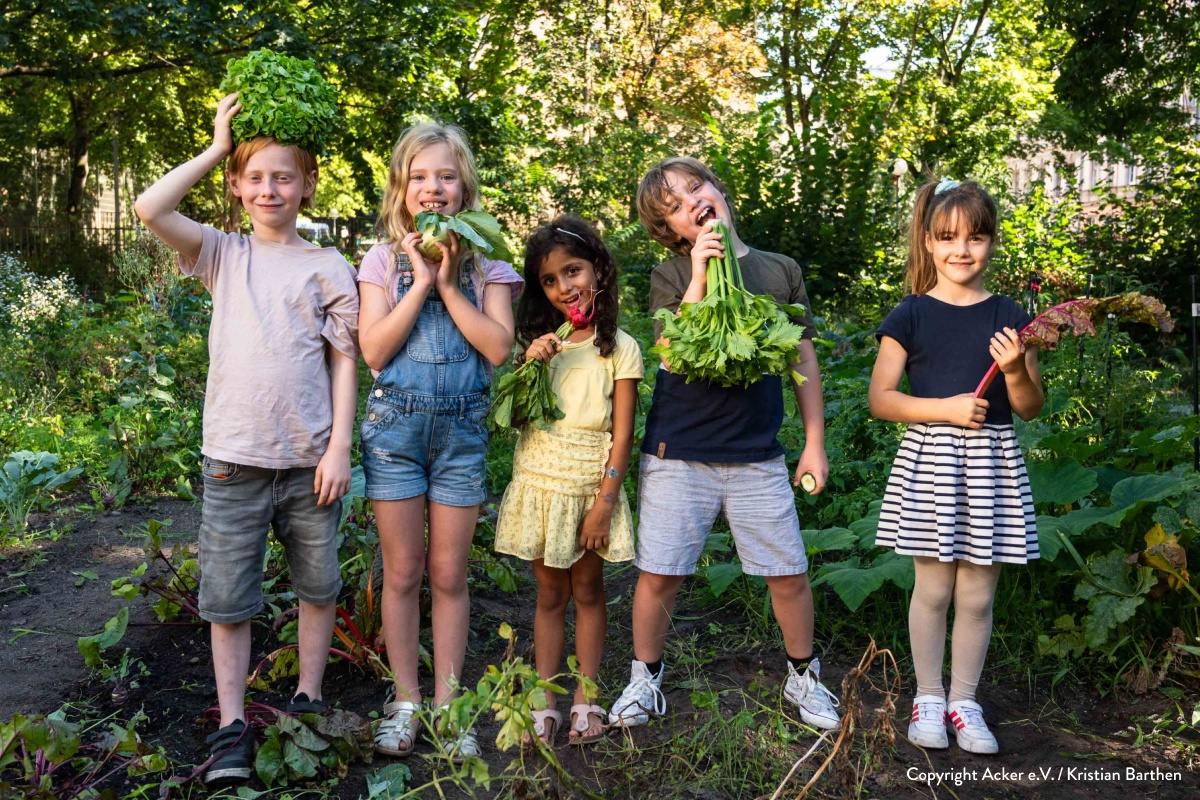 Eine Gruppe von Kindern posiert auf lustige Weise mit frisch geerntetem Gemüse auf einem Beet.