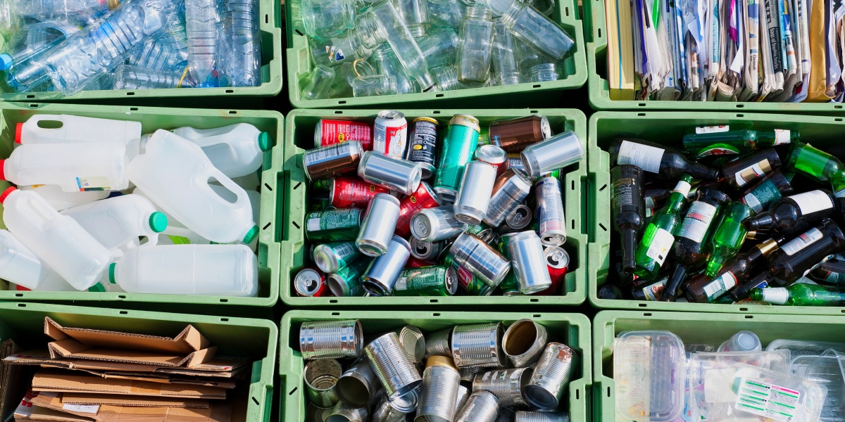 Boxen gefüllt mit recyclebaren Verpackungenen wie Getränkedosen und Glasflaschen.