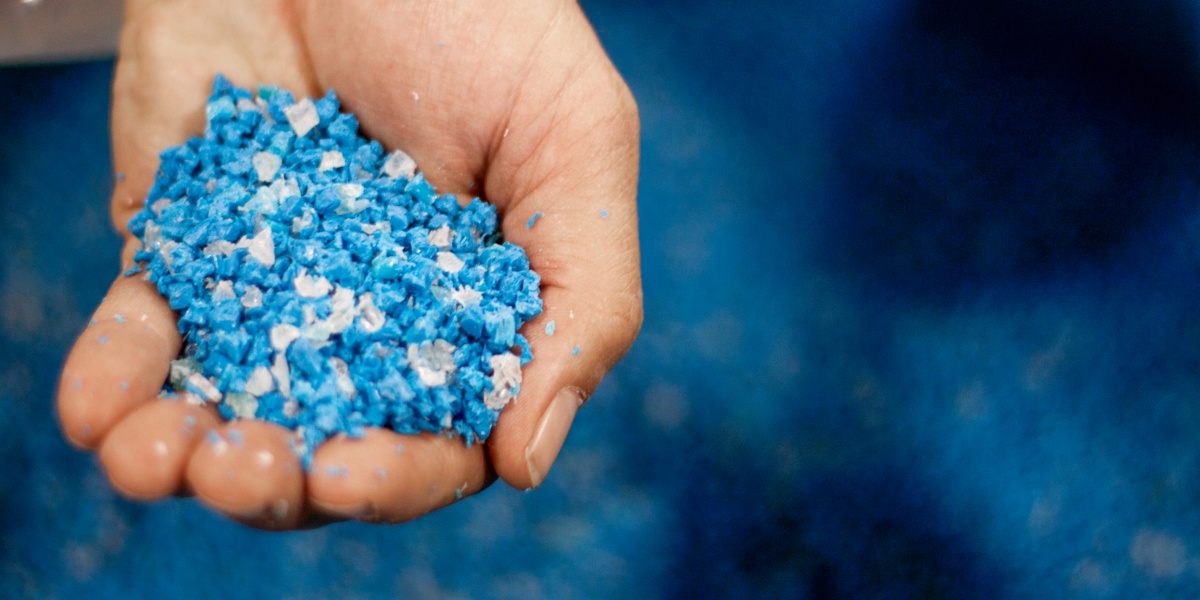 Eine Hand voller blauem und weißem recycletem Kunststoffgranulat.