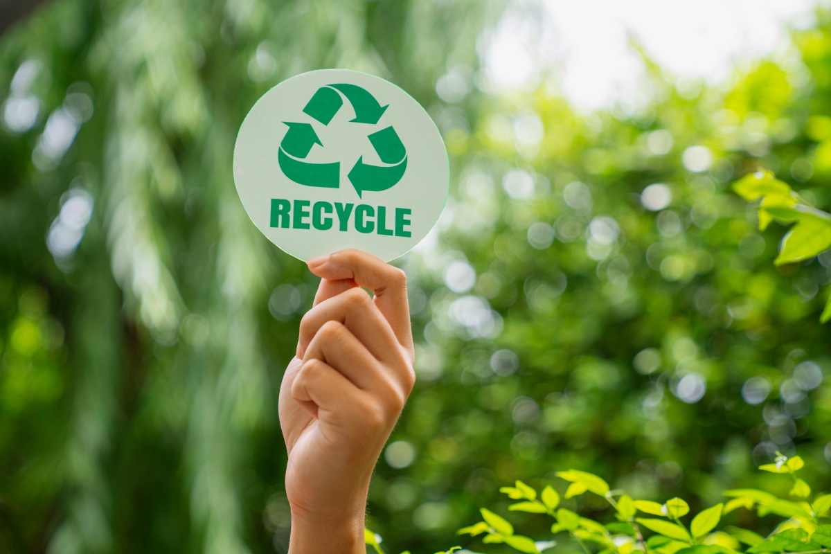 Eine Hand hält ein Schild mit der Aufschrift RECYCLE in die Höhe.